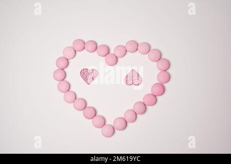 Sweets candies as heart with two glittering pink hearts on white background. Valentines day concept. Flat lay. Stock Photo