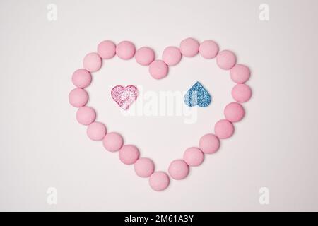 Sweets candies as heart with pink and blue glittering hearts on white background. Valentines day concept. Flat lay. Stock Photo