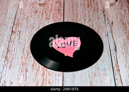 Black vinyl record with a heart in the centre on a wooden table. Stock Photo