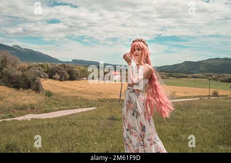 Girl in a long summer chiffon dress, wearing a pink wig and a flower crown, pictures in a flower field, with clear sky and dreamlike filter Stock Photo