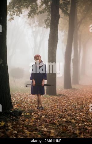 A woman with an umbrella walks in the park in foggy weather. Stock Photo