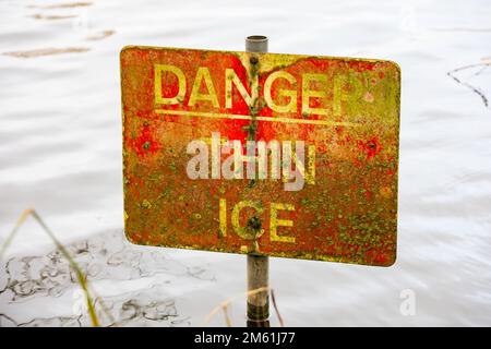 'Danger thin ice' warning sign in water. The sign is faded and has a covering of lichen moss. Stock Photo