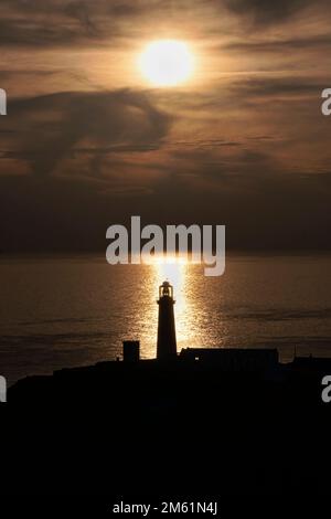 South Stack Lighthouse silhouetted at sunset against the Irish Sea, South Stack, Anglesey, North Wales, UK Stock Photo