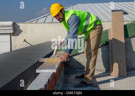 The builder is hitting the marble with a hammer and leveling it with a spirit level. The master replaces a polished marble handrail. Stock Photo