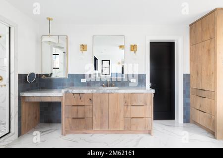 A luxurious bathroom with a wood vanity cabinet, blue tiles on the walls, gold accented lights and mirrors, and a large walk-in shower lined with marb Stock Photo