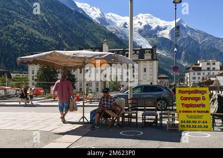 An artisan upholsterer fixing a chair at the street market of Chamonix with the Mont Blanc Massif in the background in summer, Haute Savoie, France Stock Photo