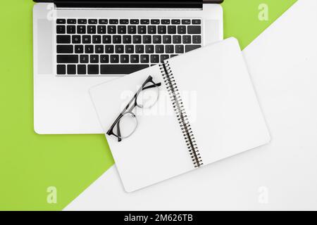 Laptop and blank notepad on color background, flat lay, workplace concept. Stock Photo