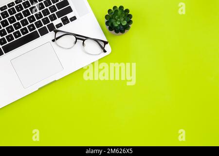 Laptop and glasses on a green background, flat lay. Stock Photo