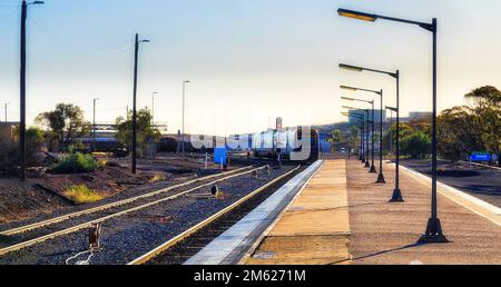 Passenger Train Broken Hill station leaving on track to sunset. Stock Photo