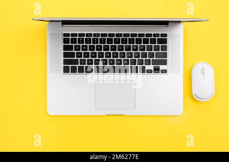 Laptop and computer mouse on yellow background, flat lay. Stock Photo