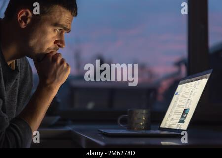 A man works on a laptop early in the morning at dawn in the dark. Stock Photo