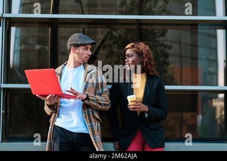 Colleagues using a laptop and talking about work while standing outside the office building. Stock Photo