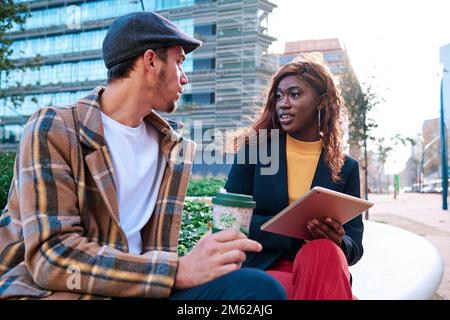 Two colleagues talking about work while sitting outdoors. Stock Photo
