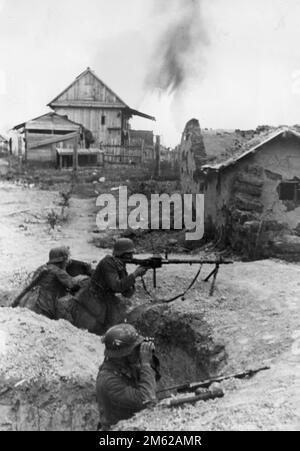 Three German soldiers (one of them with an MG-34 rifle) in a trench among village buildings near Stalingrad during the WW2 Battle of Stalingrad Stock Photo