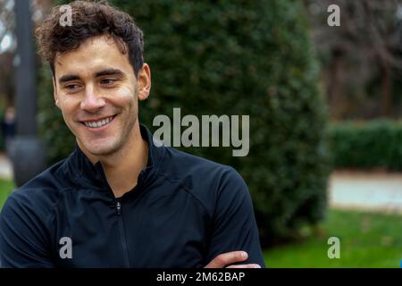 Positive young man in black shirt looking away dreamily against blurred background of green park Stock Photo