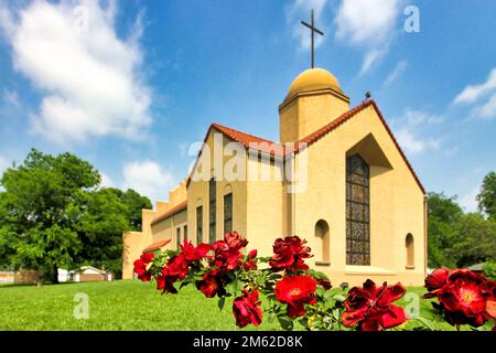The modern Mission Revival style Good Shepherd Catholic Mission church in Marietta Oklahoma with a branch of red roses in front. Stock Photo