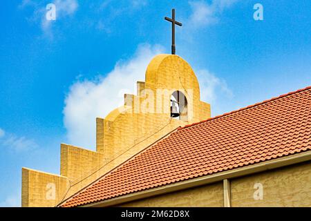 A close up view of the cross, bell, and facade on the red-tiled roof of the Good Shepherd Catholic Mission in Marietta Oklahoma. Stock Photo