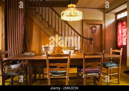 Long antique brown stained wooden dining table and chairs in dining room with tiffany lamp inside old 1838 Canadiana fieldstone home. Stock Photo