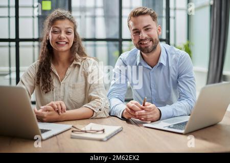 Attractive man and charming woman is pointing at the laptop screen, laughing together, resting Stock Photo