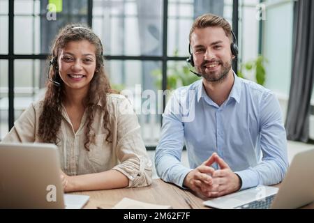 smilling man and charming woman are sitting at laptops in headphones Stock Photo