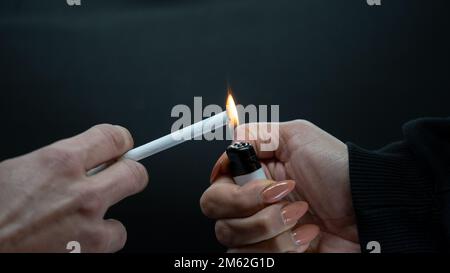 man holding a cigarette on a black background. burning cigarette with lighter Stock Photo