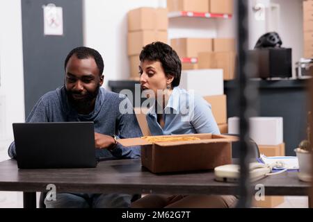 Workers looking at cargo stock on laptop after finishing packing trendy clothes in cardboard boxes before delivering to clients working in warehouse. Concept of heavy industry manufacturing factory. Stock Photo