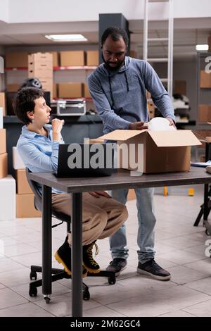 Storehouse team preparing clients packages putting order in cardboard box wrapped with bubble wrap while discussing shipping detalies, Diverse workers working in delivery department in warehouse Stock Photo