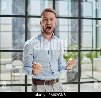 Portrait of a young businessman in a blue shirt shaking his fists celebrating his success Stock Photo