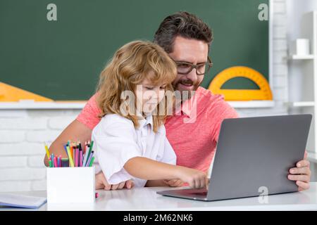 School teacher and child pupil learning at laptop computer, studying with online education e-learning in class. Teacher helping child student pupil Stock Photo
