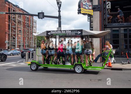 Women in blue jean shorts tour downtown Nashville on a party bar bike, a multi-passenger human-powered vehicle. Stock Photo