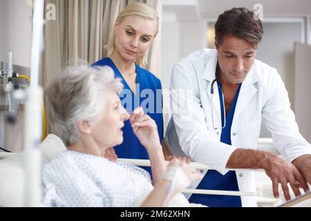 Recovering well. A doctor and his young nurse talking with their patient her medical report while standing over her bed. Stock Photo
