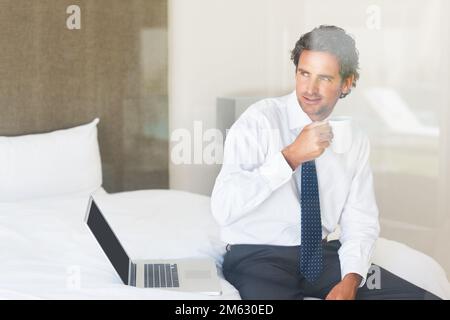 Coffee and laptop. Smart mature man with a cup of coffee and laptop on bed. Stock Photo