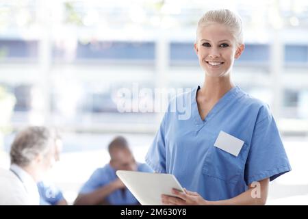 Smart technology makes efficient doctors. Medical professional standing and using a touchpad with colleagues sitting in the background. Stock Photo