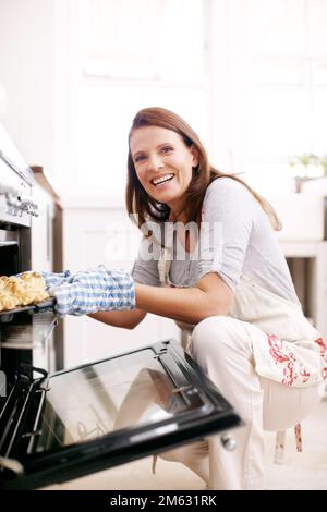 Happy at the sight of first successful scones. Portrait of a mature woman removing scones from the oven. Stock Photo