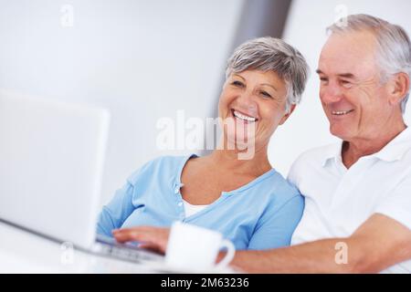 Smiling couple using laptop at home. Smiling mature woman and man using laptop at home. Stock Photo