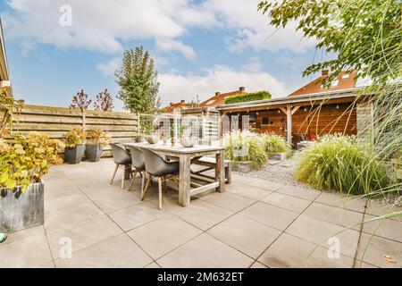 an outdoor patio with table, chairs and potted plants in the background is a blue sky filled with white clouds Stock Photo