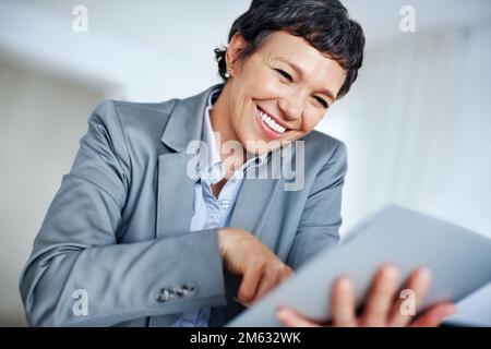 Happy business woman using digital tablet. Happy mature female executive smiling while using digital tablet in office. Stock Photo
