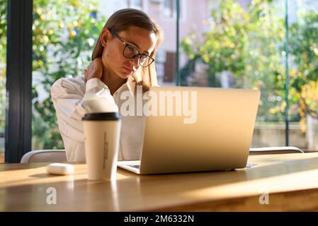 Exhausted businesswoman stretching with arms raised while working in coworking office. Stock Photo