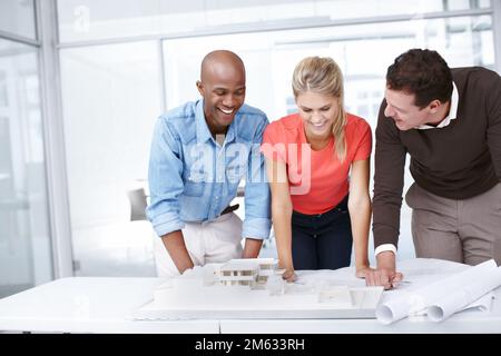 Putting their ideas on the table. Three architects standing by an architectural model and discussing it. Stock Photo