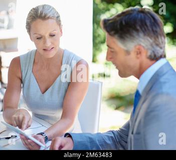Their ideas turn to business gold. two mature businesspeople talking together of a digital tablet. Stock Photo