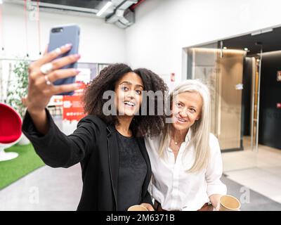 Positive colleagues taking selfie during break from work at office Stock Photo