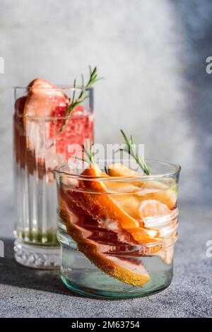 Summer tropical cocktail of vodka and sprite with ripe fruits and rosemary on grey background Stock Photo
