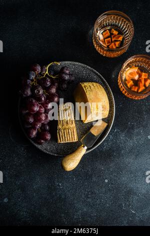 Black stone plate with cheeses, raw tasty grape and glasses of wine on dark concrete table Stock Photo