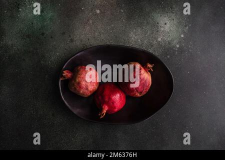 From above organic whole pomegranate fruits with its seeds on black stone background Stock Photo