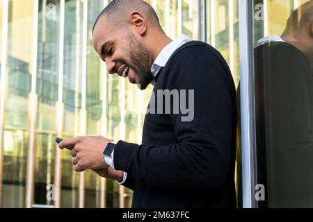 Low angle of side view bearded African American male entrepreneur in smart casual apparel standing against contemporary glass chatting on mobile phone Stock Photo