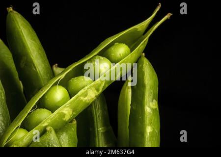 Bunch of ripe green pods with fresh peas against black background Stock Photo