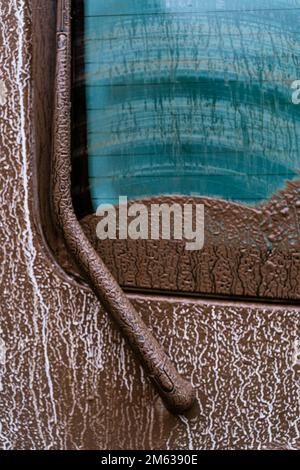 Muddy rear car window with wiper covered by water drops on rainy day Stock Photo