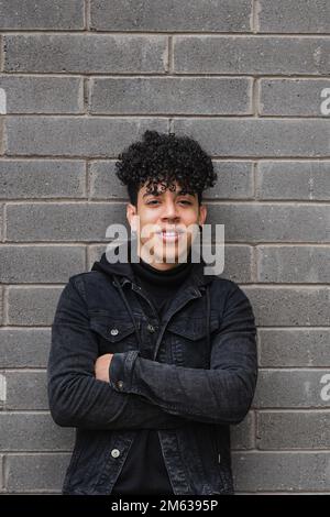 Portrait of smiling young ethnic curly haired man in casual outfit standing with crossed arms looking at camera Stock Photo