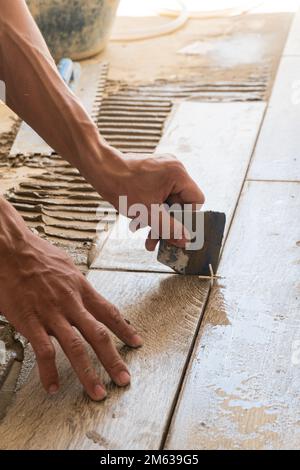 From above of crop anonymous male master holding metal piece and leveling tile during renovation on sunny day Stock Photo