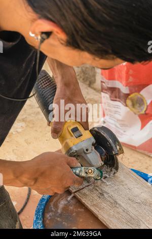 High angle of crop dark haired repairman in earphones cutting tile with disk grinder while listening to music Stock Photo